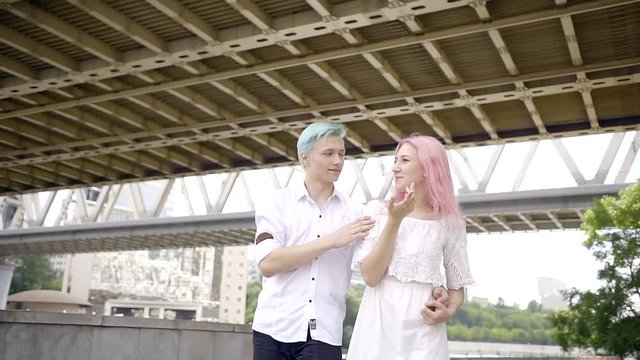 Young European tourists take a walk along the river of a big city. Hold each other gently over their hand very well together. Dressed in comfortable white clothes. hair dyed in bright colors