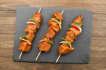 From above stone board with raw meat skewers with vegetables.