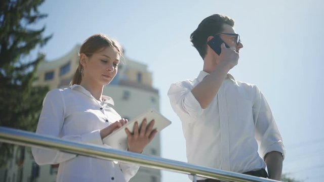 Man woman outside using holding phone tablet talking showing tapping touching screen smart casual wear business partners discussing ideas team looking nodding head agreement thoughtful attractive pair