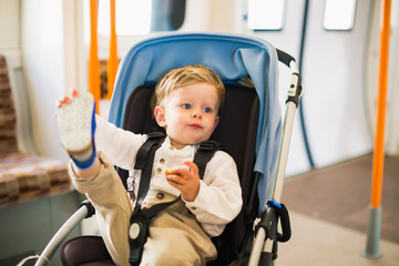 The little cute boy sits in pram in a bus and eats cake