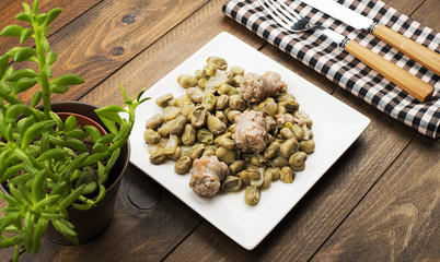 From above plate with cooked beans and sausage served on wooden table near a plant.