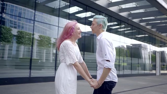 slim happy young couple having fun walking in the modern city by day in Sunny weather. wear white comfortable clothing. hair dyed in bright colors