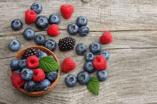 mix of blueberries, blackberries, raspberries in wooden bowl on old wooden table background. top view with copy space