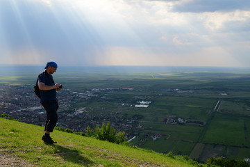 A young man standing on a hill and photographing amazing view of the plain