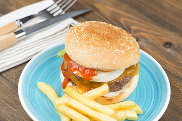 Tasty homemade burger served with fries on plate on a table next to cutlery.
