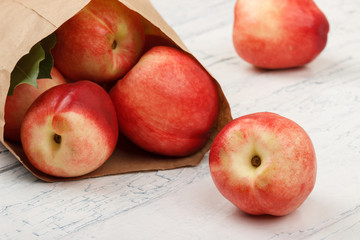Ripe red peaches in the paper bag on the white wooden table