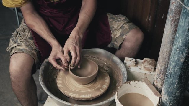 Potter shapes the clay product with pottery tools on the potter's wheel, top view, toned cinematic, craft factory authentic