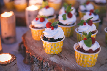 Cupcakes with berries on a wooden shelf in candle light