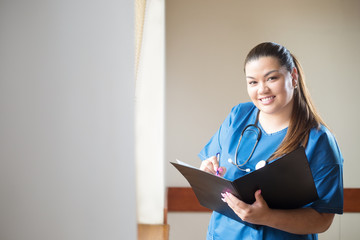 Young hispanic nurse smiling, holding a report and looking into folder she is holding in her hands