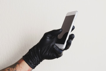 Tattooed man in black glove using white smartphone
