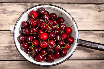 Cherry in enameled metal colander on wood table