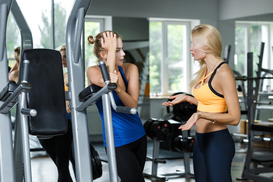 Two athletic blond women talking in the gym. Girl communicates with trainer