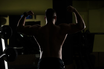 Fototapeta na wymiar Siluet Muscular Man Flexing Muscles In Gym