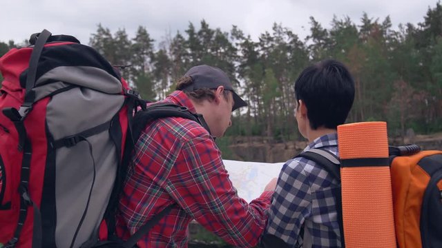 Happy friends looking on the map and choose the direction of the path. couple climbers with backpack discussing the way. Smiling tourists in forest with beautiful nature.