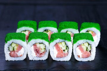Delicious sushi roll with pink salmon, decorated with caviar, served on black stone slate. Japanese restaurant menu