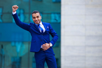 Young attractive business man in suit celebrating success on office building background, copy space