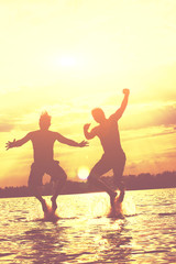 Fototapeta premium Glückliche junge Menschen laufen und springen am See beim Sonnenuntergang