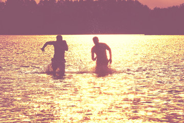 Glückliche junge Menschen laufen und springen am See beim Sonnenuntergang