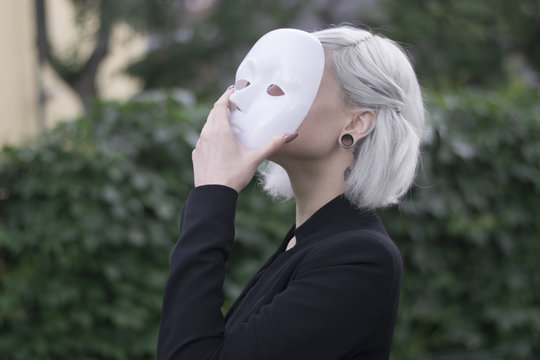 Young Blond Woman Taking Off A Mask. Pretending To Be Someone Else Concept. Outdoors.