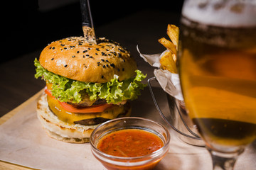 Burger with fried potatoes and tomato sauce on a wooden stand with a glass of beer