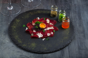 Italian Delicious Antipasto bresaola with oregano, quail egg, onion on stone plate, top view