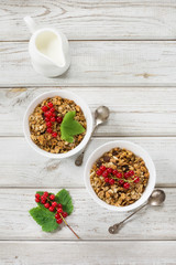 Summer healthy breakfast for two person of granola, muesli with milk jug with red currant decor on light wooden board.