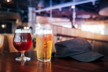 Two glasses of light and dark beer on a wooden table with a black cap in a cafe or restorant