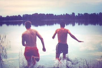 Glückliche junge Menschen laufen und springen am See beim Sonnenuntergang