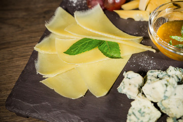 Cheese mix with honey and grapes on a stone background