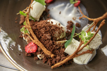 Ice cream dessert with raspberries, chocolate chips and greenery on a brown plate.