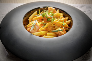 Penne pasta with salmon and cheese cream on a black plate.