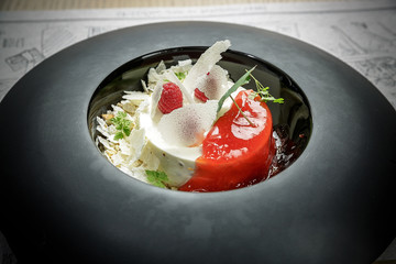 Ice cream dessert with raspberries, jelly and greenery on a black plate.