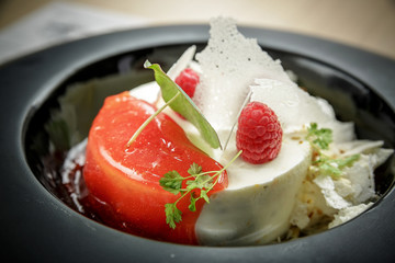 Ice cream dessert with raspberries, jelly and greenery on a black plate.