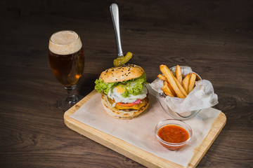 Burger with fried potatoes and tomato sauce on a wooden stand with a glass of beer