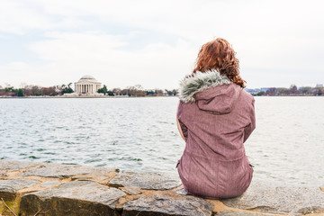Young woman sitting on edge looking over Tidal Basin and Thomas Jefferson Memorial in park