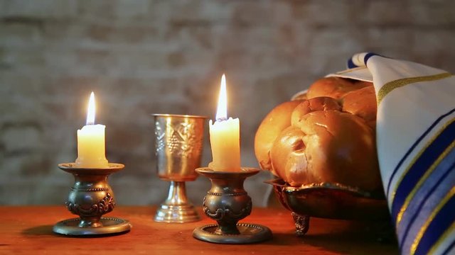 Shabbat candles in glass candlesticks with blurred covered challah background.