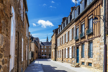Beautiful view of scenic narrow alley with historic traditional houses and cobbled street in an old town of Dinan with blue sky and clouds. Brittany (Bretagne), France