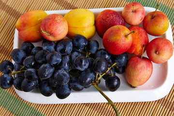 Naklejka na ściany i meble Bunch of black grapes and peaches on a rectangular plate