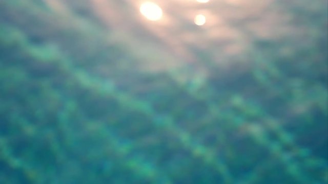 Background of the undulating surface of the pool water. The rays of the sun are reflected in the water. Beautiful sparkling bokeh on the water play a bright light