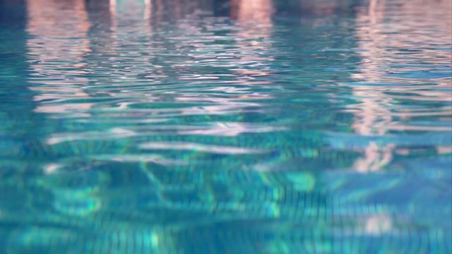 Background of the undulating surface of the pool water. The rays of the sun are reflected in the water. Beautiful sparkling bokeh on the water play a bright light