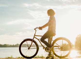 Young woman on a bicycle on the beach on a sunset background
