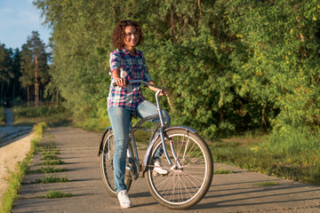 Fototapeta na wymiar Young woman on a bicycle in the park on a sunset background 