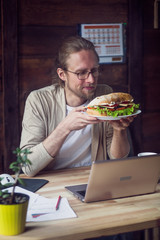 Freelancer at home office, having lunch. Man holding plate with sandwiches in his hands. Toned image.
