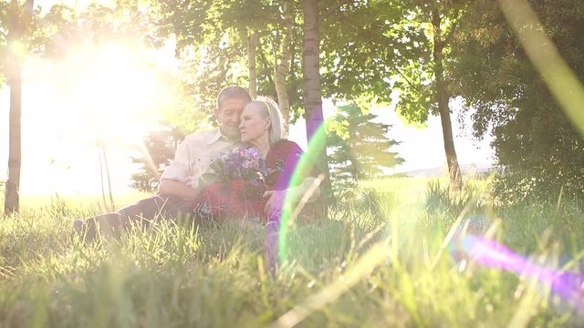 Mature couple sitting in a hug on the grass in the park in the light of a bright sun.