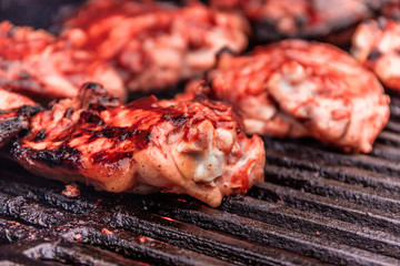 Grilled seasoned chicken thighs cook on a cast iron barbecue grill with fresh BBQ sauce