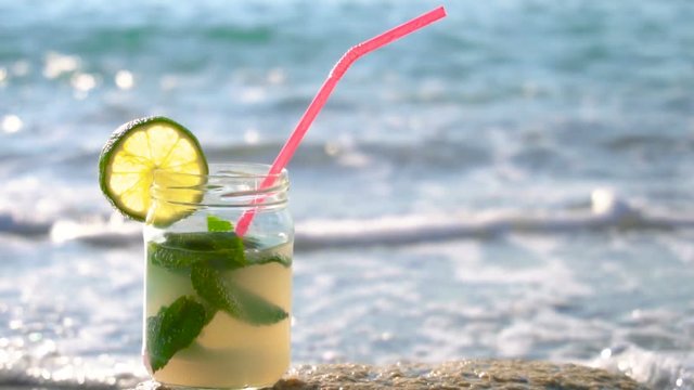 Close up of glass of mojito alcoholic cocktail standing in the sand on a beach