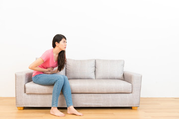 young woman sitting on sofa making pain gesture