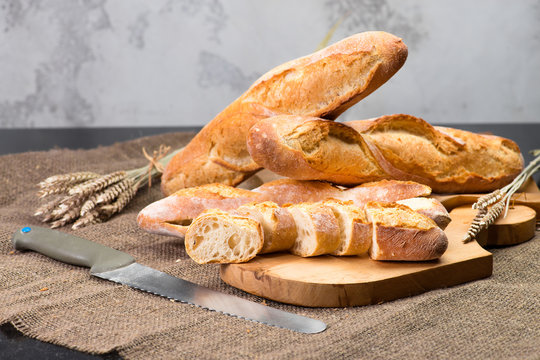 still life with French fresh bread baguettes with poolish on a wooden cutting board, knife and wheat, shallow dof