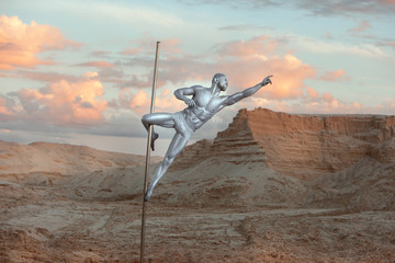 Man is engaged in Pole Dance on a pole in the desert sands.