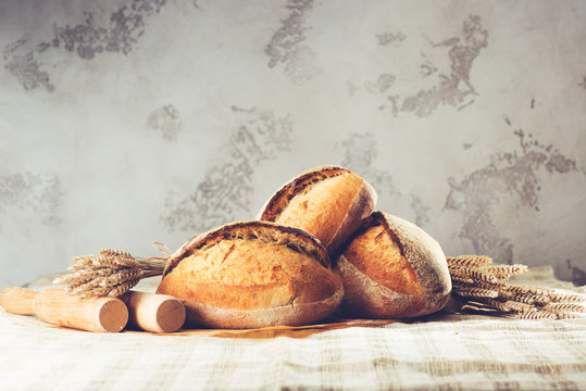 still life with a traditional round artisan wheat bread loaves, wheat and pestles on light textile background. Shallow dof, toned image